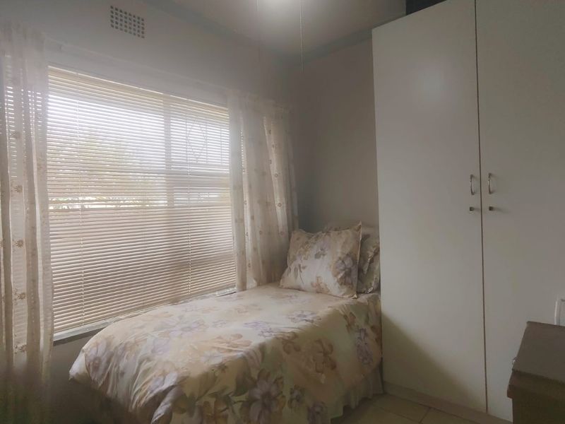 A functional bedroom featuring tiled flooring, a ceiling fan, and a built-in wardrobe, providing essential storage and comfort.