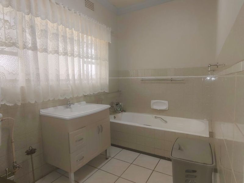 A functional bathroom featuring a built-in vanity, bathtub, and tiled wall and floor finishes, offering a dated aesthetic ready for modernization.