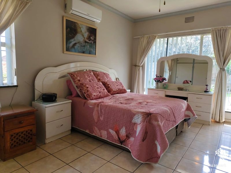 A well-lit bedroom featuring tiled flooring, a wall-mounted split-system air conditioner, and large windows with access to the exterior.