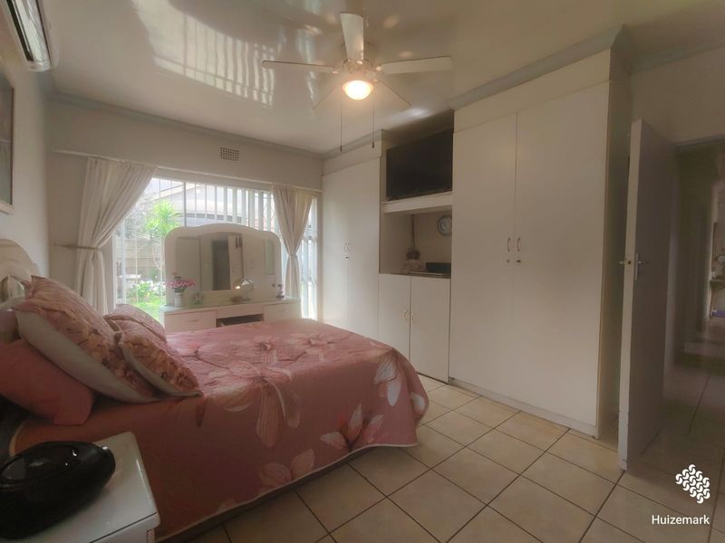 A bedroom featuring tiled flooring, built-in cupboards, a ceiling fan, and an air conditioning unit, with direct access to the garden area.