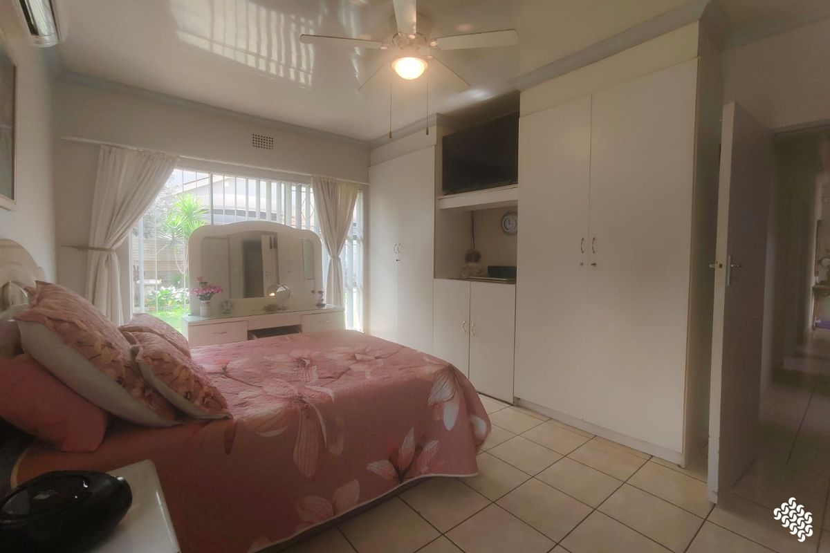 A bedroom featuring tiled flooring, built-in cupboards, a ceiling fan, and an air conditioning unit, with direct access to the garden area.
