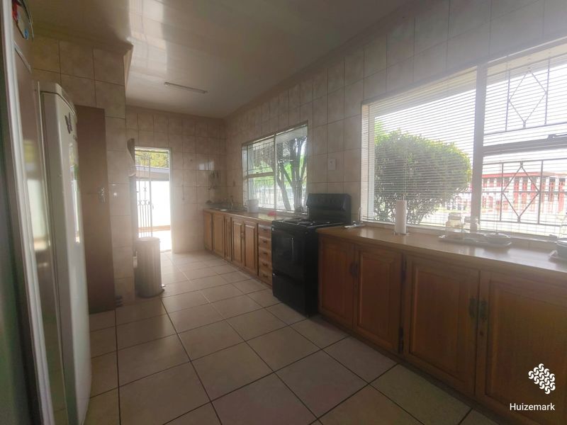 A functional kitchen featuring wooden cabinetry, tiled walls and flooring, and a freestanding stove, with natural light provided by large windows.