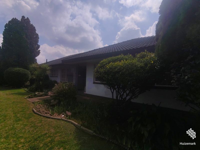Front view of a single-story residential house featuring a tiled roof, established garden, and a paved walkway leading to the entrance.