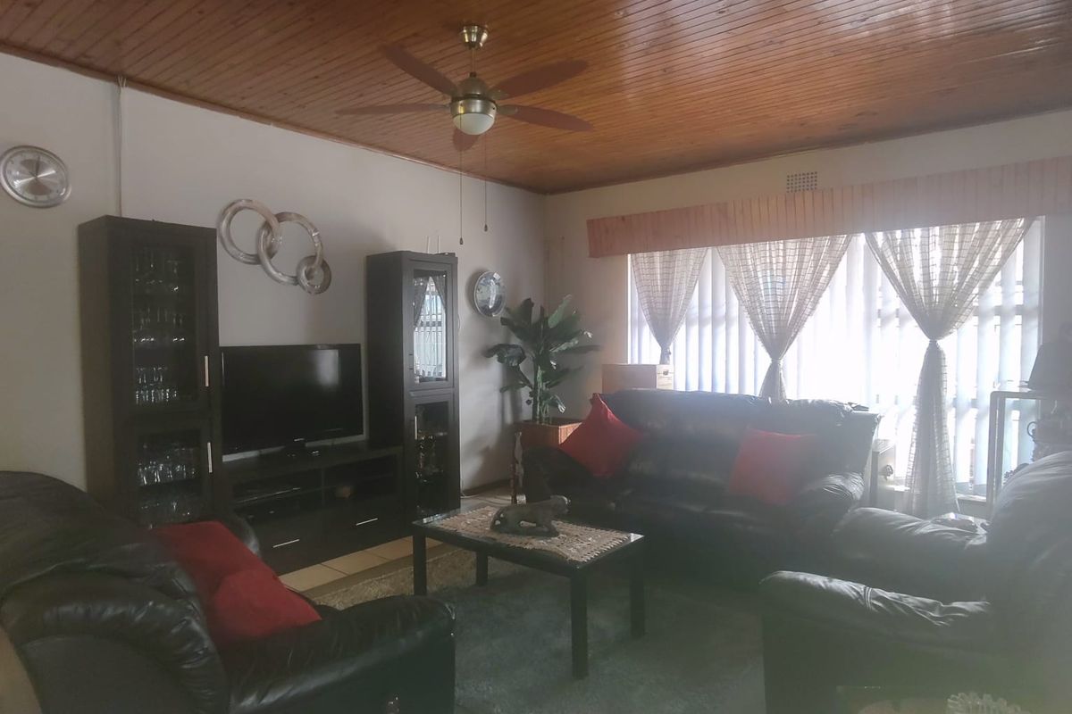 A living room featuring a timber tongue and groove ceiling, ceiling fan, and vertical blinds, offering a traditional aesthetic.