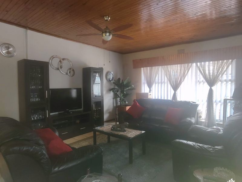 A living room featuring a timber tongue and groove ceiling, ceiling fan, and vertical blinds, offering a traditional aesthetic.