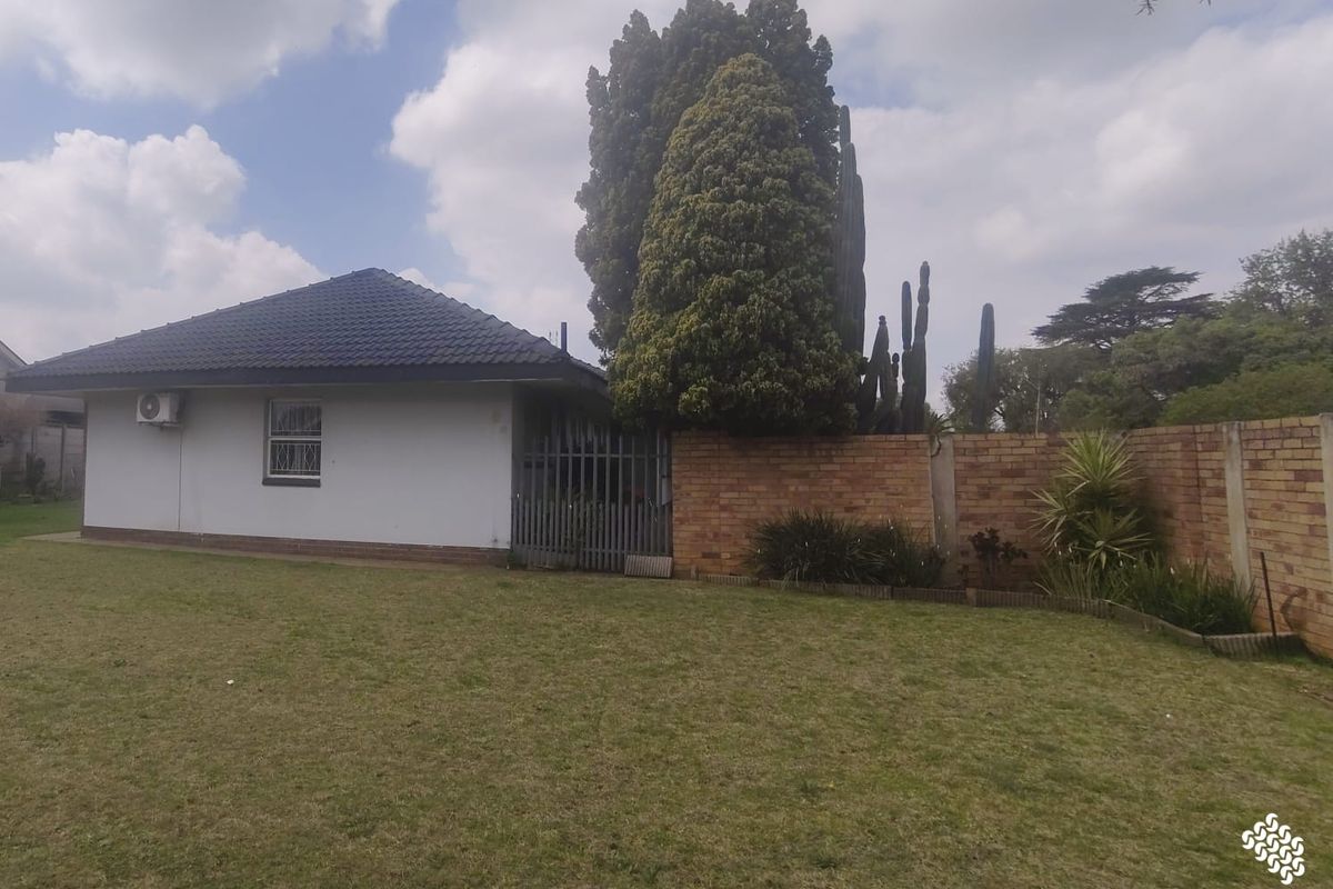 Rear view of the property featuring a tiled roof, brick boundary wall, and a well-maintained lawn area.