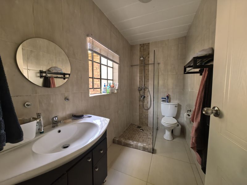 A functional bathroom featuring a vanity cabinet, walk-in shower with glass screen, and neutral wall and floor tiling.
