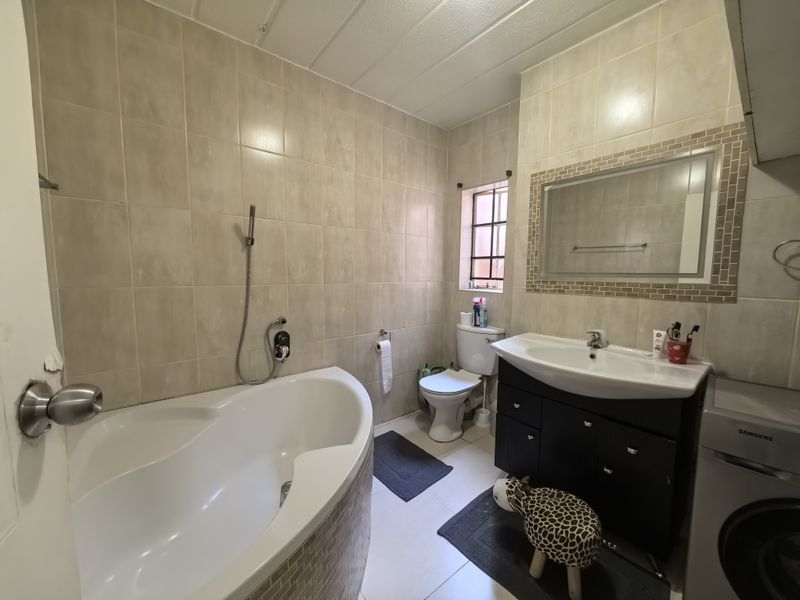 A functional bathroom featuring a corner bathtub, vanity cabinet with basin, and tiled finishes throughout.