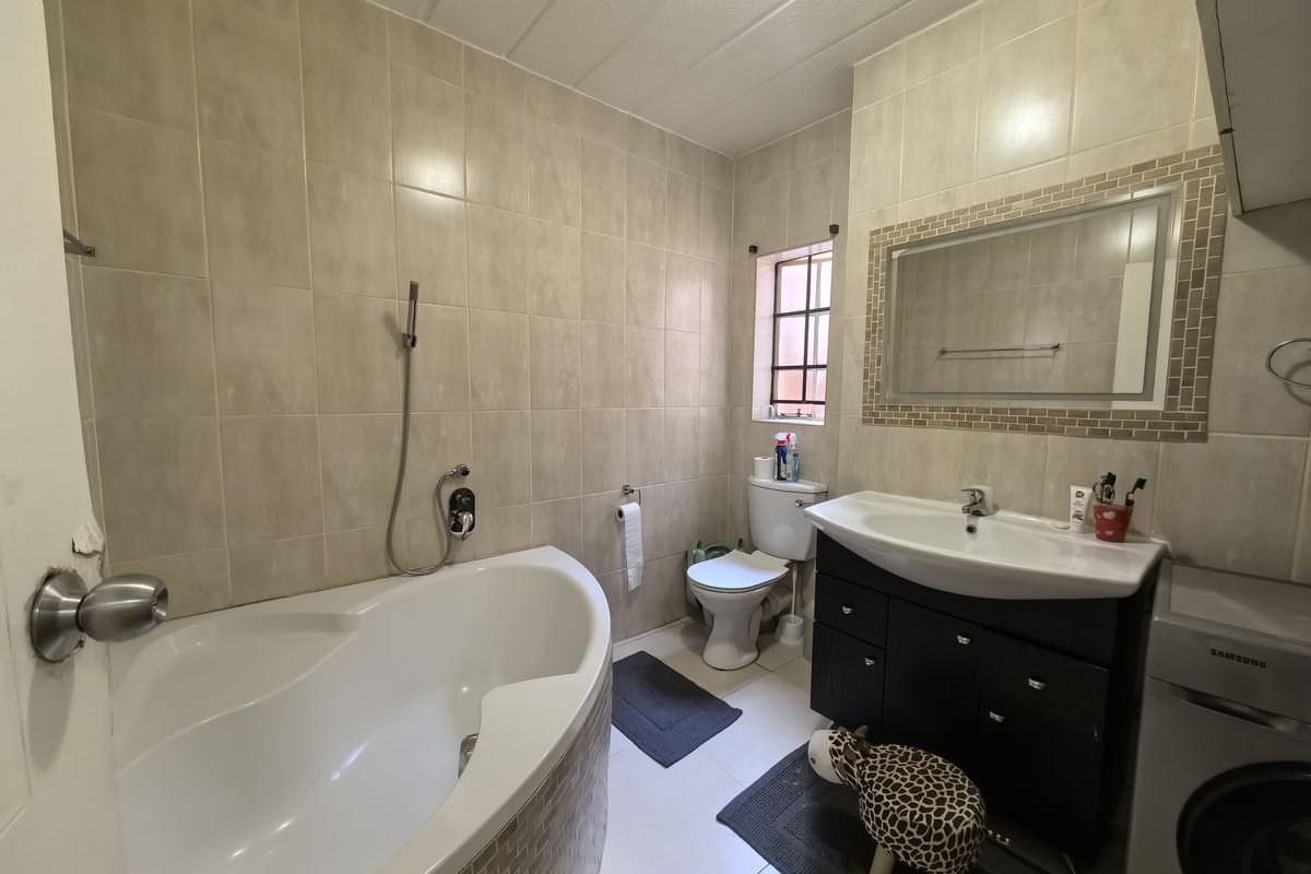 A functional bathroom featuring a corner bathtub, vanity cabinet with basin, and tiled finishes throughout.