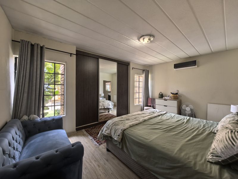 A well-lit bedroom featuring built-in mirrored wardrobes, laminate flooring, and a wall-mounted air conditioning unit, offering a comfortable and functional living space.