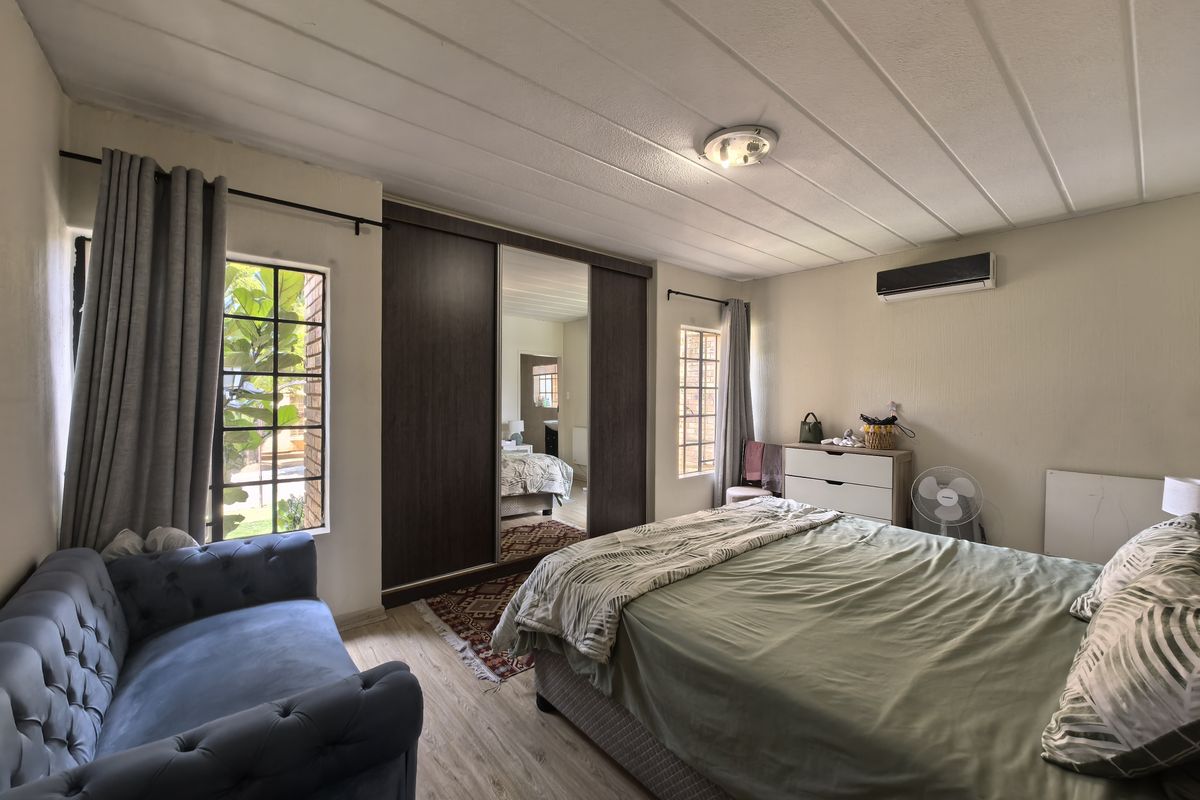 A well-lit bedroom featuring built-in mirrored wardrobes, laminate flooring, and a wall-mounted air conditioning unit, offering a comfortable and functional living space.