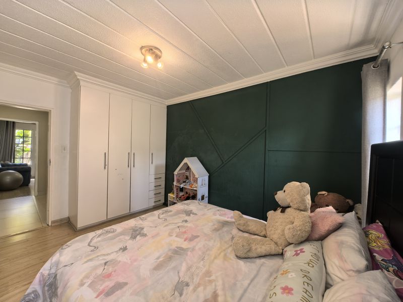 A well-maintained bedroom featuring built-in cupboards, laminate flooring, and a decorative dark green accent wall with geometric paneling.