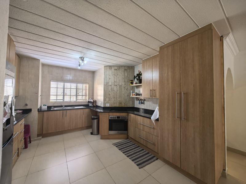 A functional kitchen featuring wood-finish cabinetry, granite countertops, a built-in oven and hob, and tiled flooring with ample storage space.