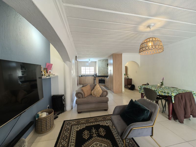 Open-plan living and dining area featuring tiled floors, an arched transition, and a functional kitchen with built-in cabinetry and appliances.