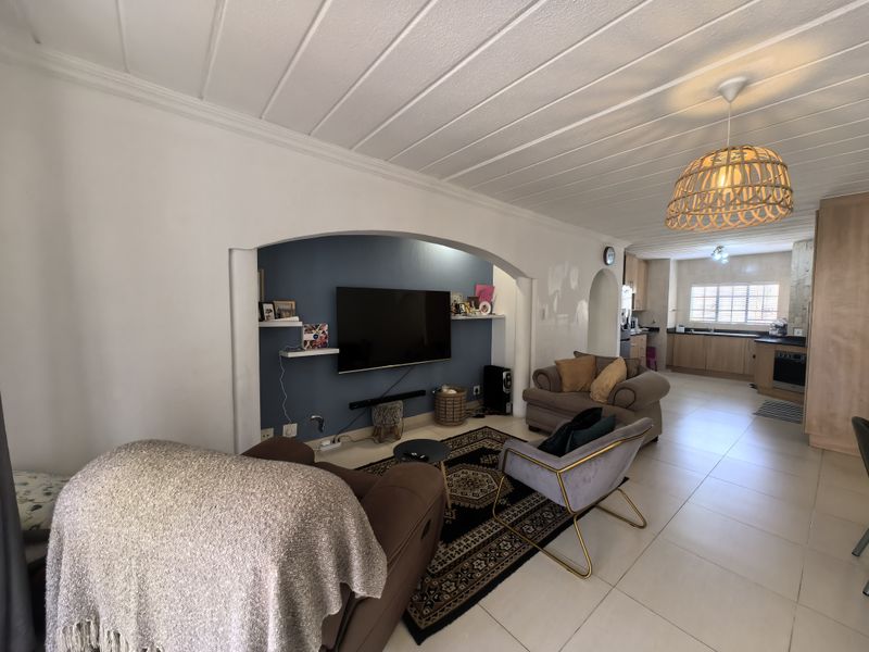 Open-plan living area featuring a distinctive arched wall niche, tiled flooring, and a connected kitchen with built-in cabinetry and appliances.