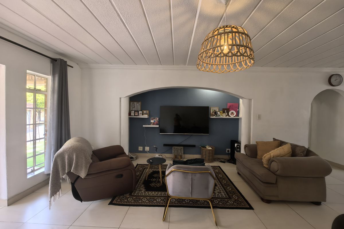 A comfortable living room featuring a distinctive arched wall niche, tiled flooring, and a classic tongue and groove ceiling with a central pendant light.