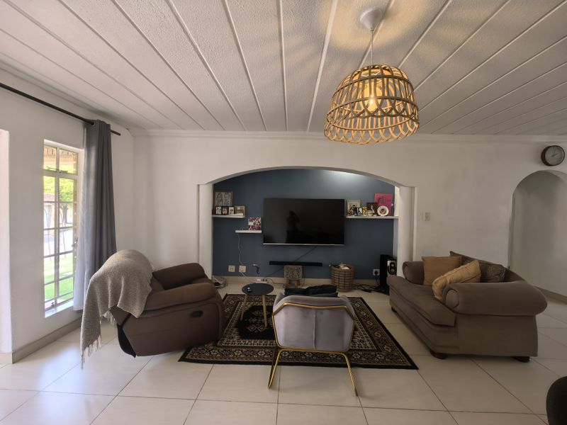 A comfortable living room featuring a distinctive arched wall niche, tiled flooring, and a classic tongue and groove ceiling with a central pendant light.