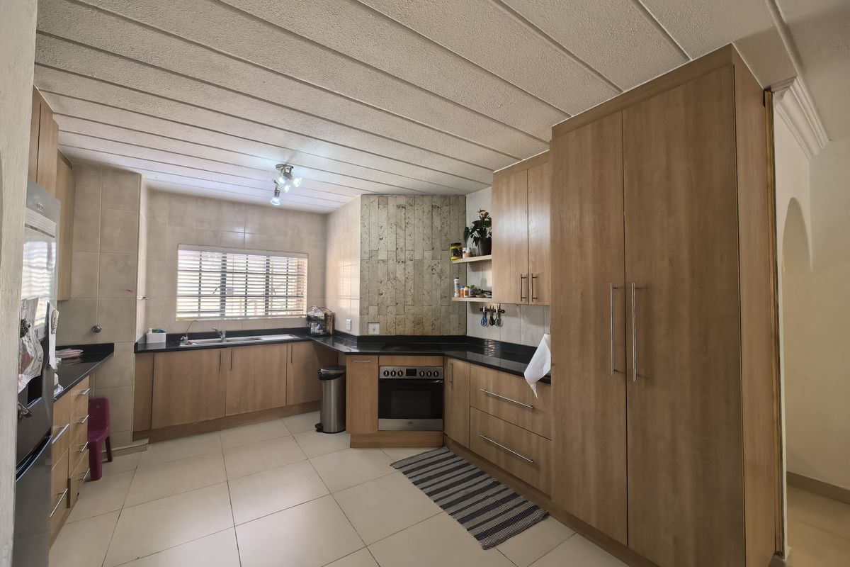 A functional kitchen featuring light wood cabinetry, granite countertops, built-in oven, hob, and tiled flooring with a neutral aesthetic.