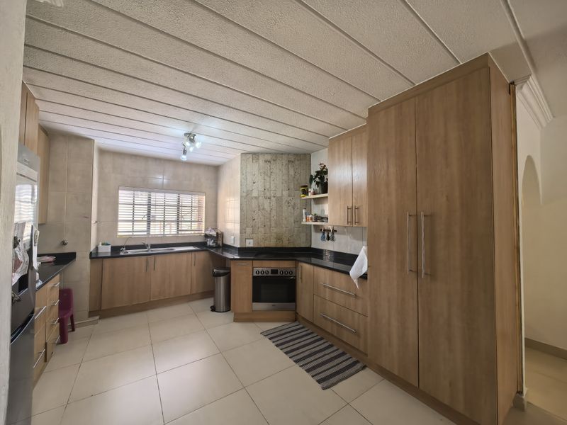 A functional kitchen featuring light wood cabinetry, granite countertops, built-in oven, hob, and tiled flooring with a neutral aesthetic.