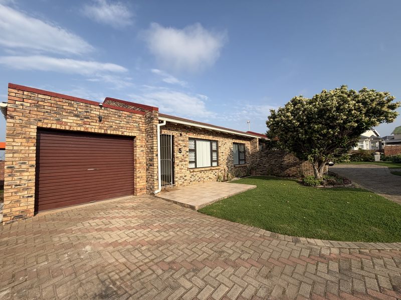 Front exterior view of a face brick townhouse featuring a paved driveway, single garage, and a small tiled entrance patio with a landscaped garden.