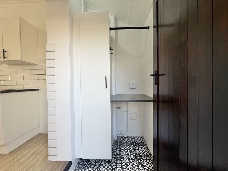 A clean and functional laundry area featuring built-in cabinetry, a laminate work surface, plumbing connections, and decorative patterned floor tiles.
