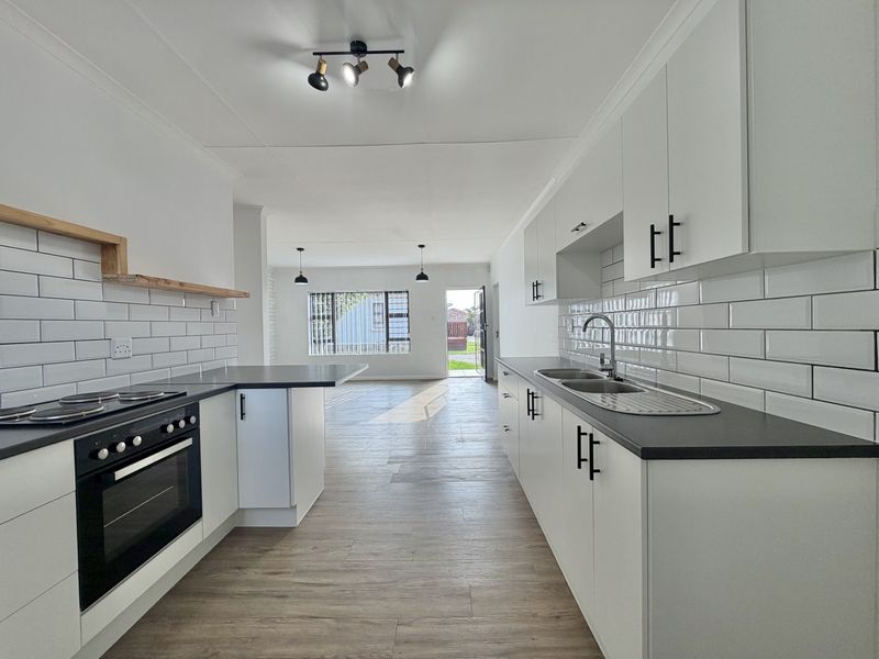 Modern open-plan kitchen featuring white cabinetry, subway tile backsplash, dark countertops, and integrated oven, flowing into a bright, empty living area.