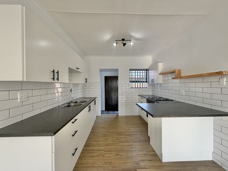 A modern, renovated kitchen featuring white cabinetry, dark countertops, subway tile backsplash, and wood-look flooring in excellent condition.