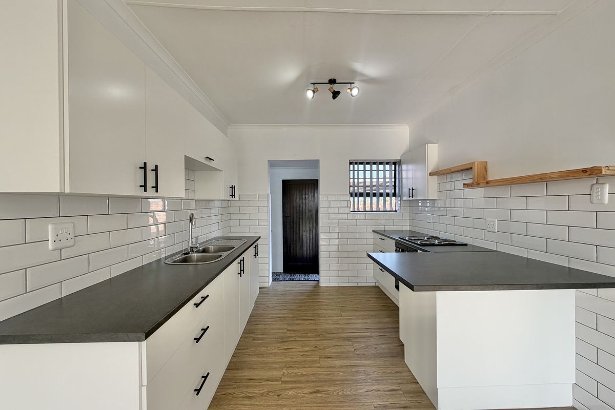 A modern, renovated kitchen featuring white cabinetry, dark countertops, subway tile backsplash, and wood-look flooring in excellent condition.