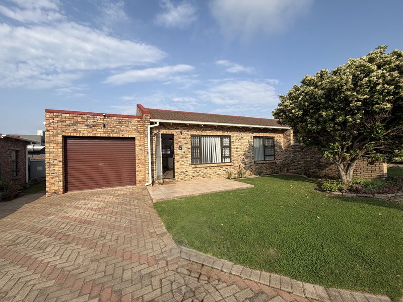 Front view of a face brick townhouse featuring a paved driveway, single garage, tiled entrance porch, and a well-maintained front garden.