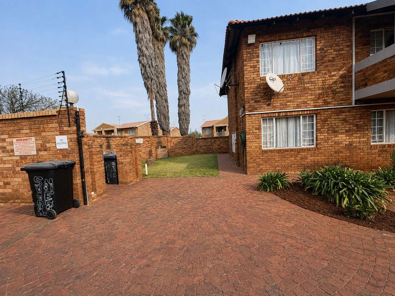 Rear exterior view of the townhouse featuring a brick facade, paved courtyard area, and perimeter security fencing.