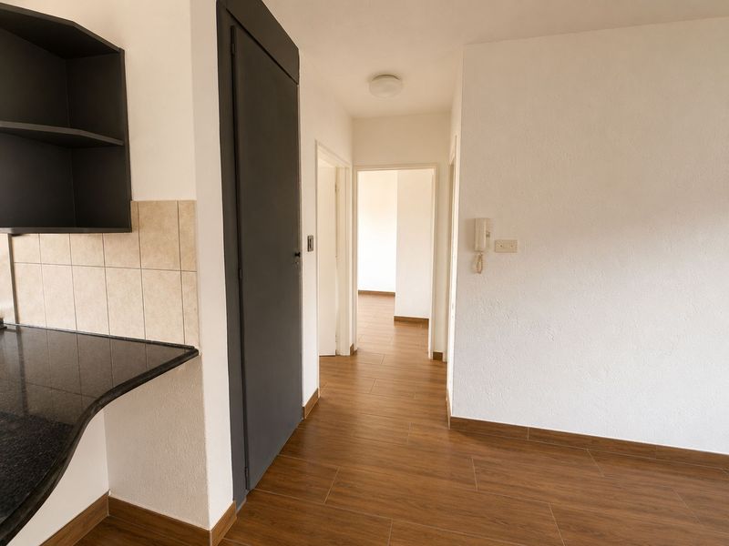 A clean, well-maintained hallway featuring wood-look tiled flooring, an intercom system, and a small adjacent kitchen prep area with dark cabinetry.
