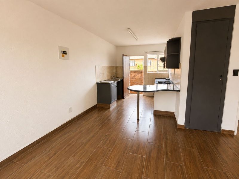 A clean, empty kitchen featuring wood-look floor tiles, built-in cabinetry with a breakfast bar, and direct access to an outdoor area.