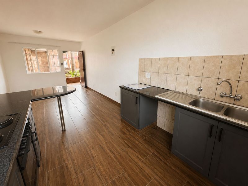 Modern kitchen featuring dark cabinetry, granite countertops, breakfast bar, and wood-look floor tiles, leading directly to an outdoor patio area.