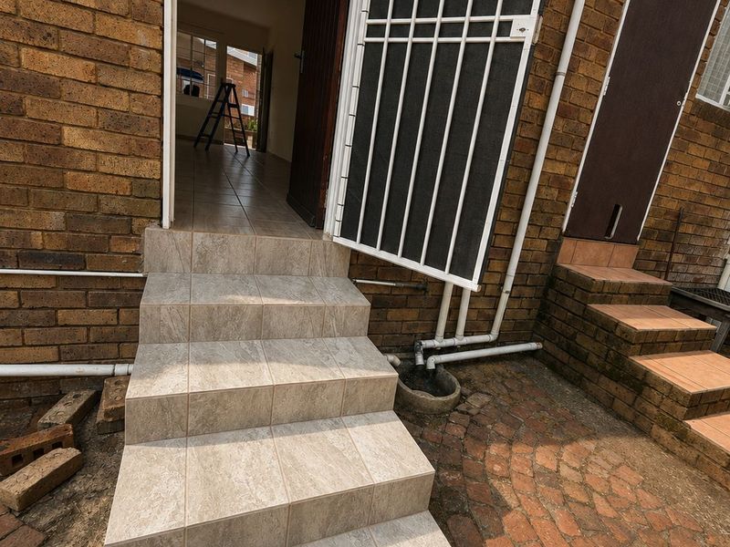 Rear exterior view of a townhouse featuring tiled steps leading to an entrance, a security gate, and a paved courtyard area.