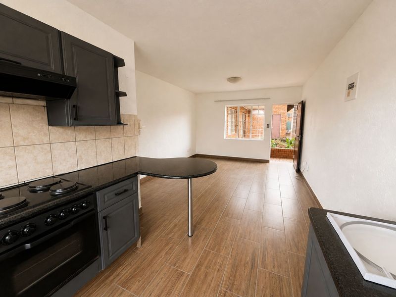 Open-plan kitchen and living area featuring dark cabinetry, granite countertops, integrated stove, and wood-look tiled flooring with direct access to the rear exterior.