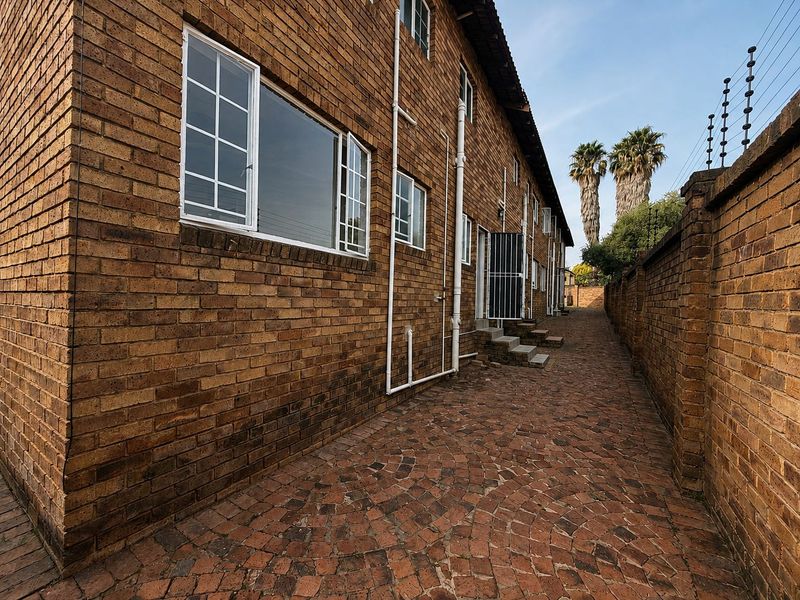 A side view of the townhouse featuring a face brick exterior, paved walkway, and secure boundary wall with electric fencing.