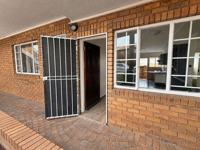 Front entrance of the townhouse featuring a paved patio, face brick exterior, security gate, and timber front door with views into the interior living space.