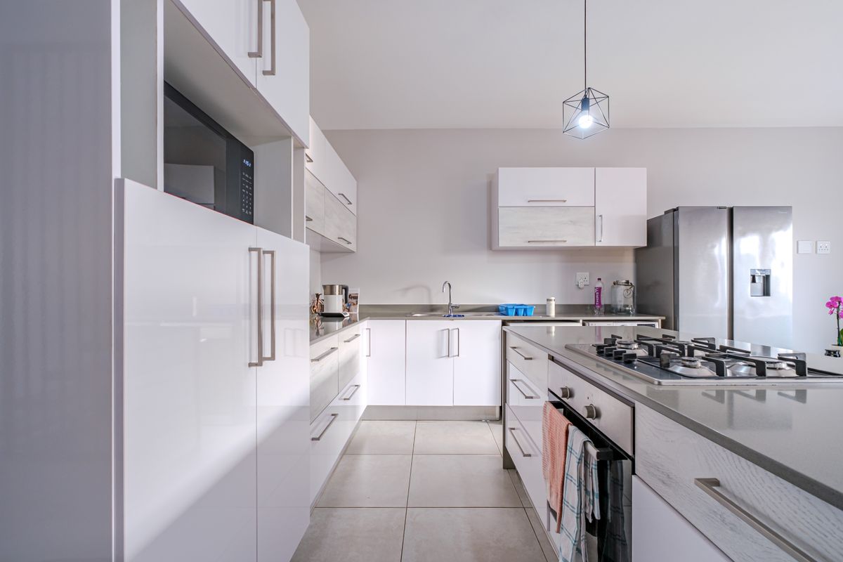 Modern kitchen featuring white cabinetry, stone countertops, a gas hob, built-in oven, and integrated microwave, complemented by neutral tiled flooring.