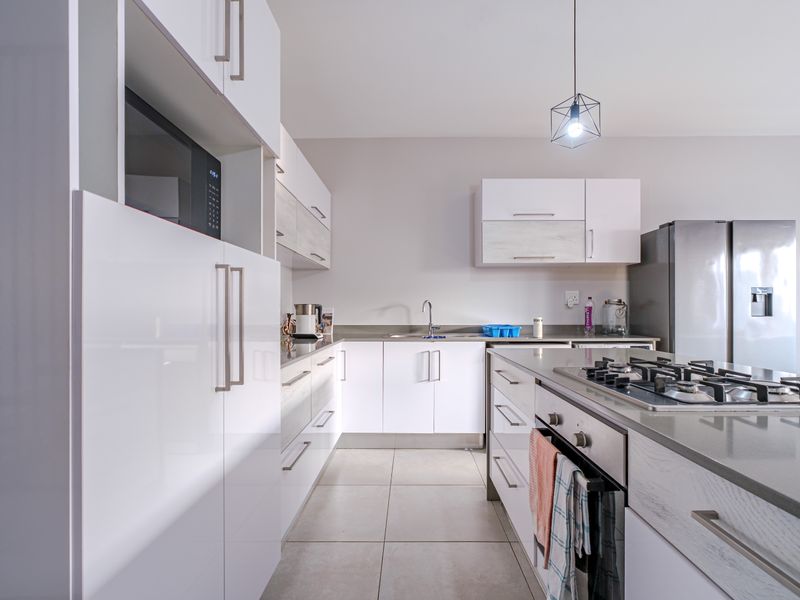 Modern kitchen featuring white cabinetry, stone countertops, a gas hob, built-in oven, and integrated microwave, complemented by neutral tiled flooring.