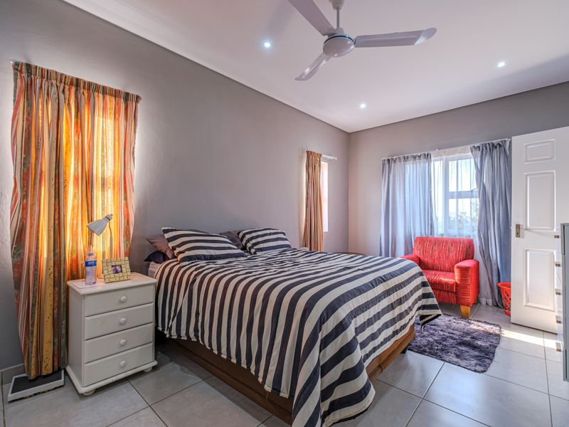 A well-lit bedroom featuring neutral grey walls, tiled flooring, a ceiling fan, and recessed lighting, providing a comfortable and functional living space.