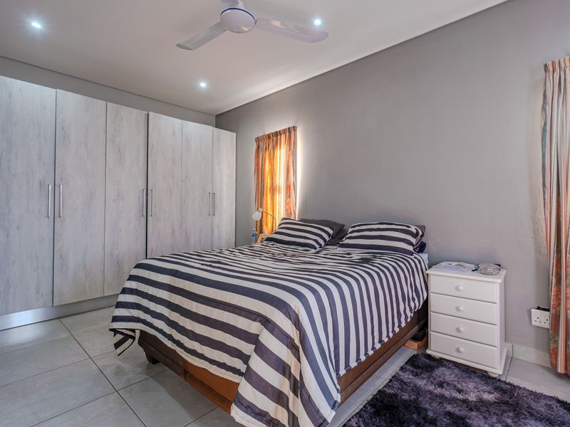 A well-maintained bedroom featuring built-in cupboards, tiled flooring, a ceiling fan, and recessed downlighting.