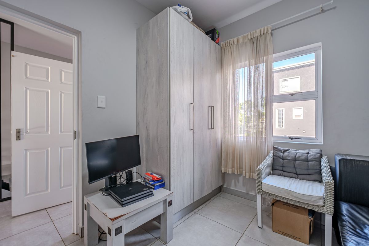 A compact bedroom featuring neutral tiled flooring, a built-in wardrobe with light wood-grain finish, and an aluminium-framed window allowing natural light.