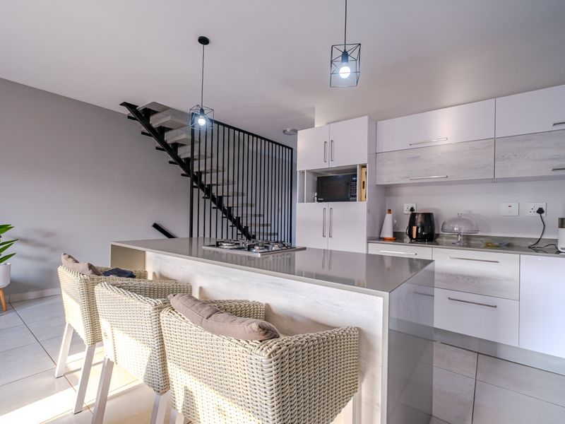Modern open-plan kitchen featuring a central island with built-in hob, sleek cabinetry, and an adjacent staircase with a contemporary metal balustrade.