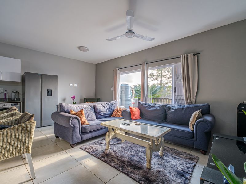 Open-plan living area featuring tiled flooring, a ceiling fan, and an integrated kitchen space with direct access to an outdoor area.