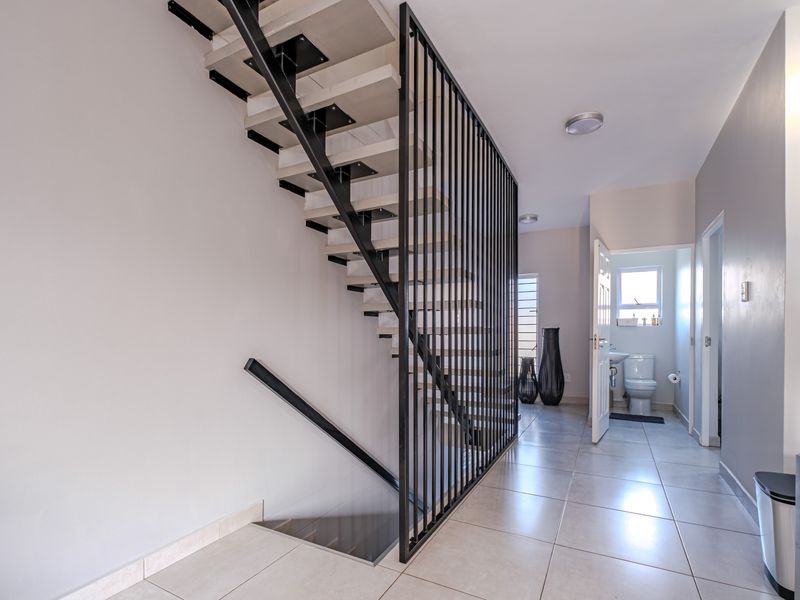 A bright, modern hallway featuring a contemporary open-tread staircase with a sleek black metal balustrade and neutral floor tiling.