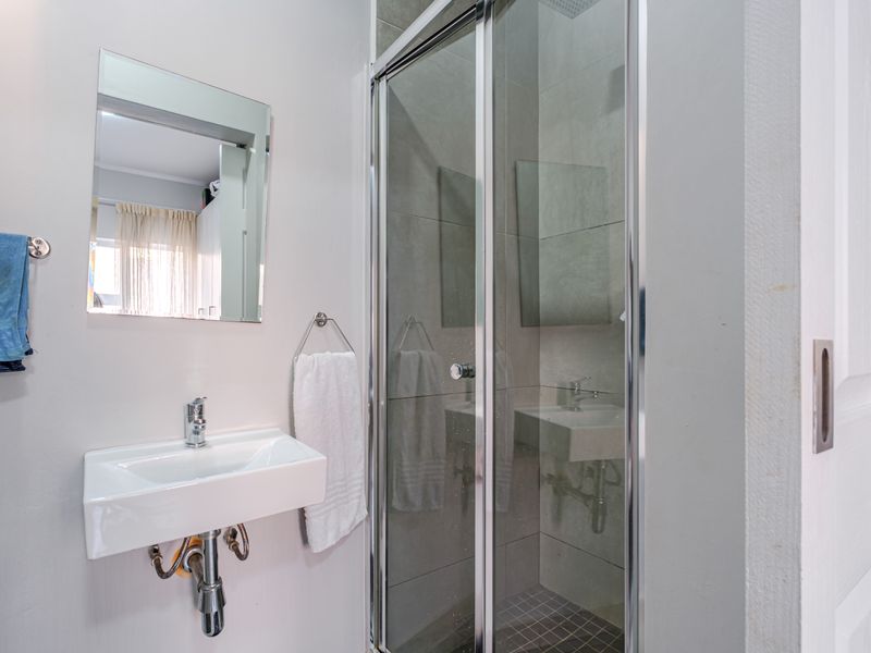 A compact, modern bathroom featuring a wall-mounted basin with chrome fixtures and a glass-enclosed shower with tiled flooring.