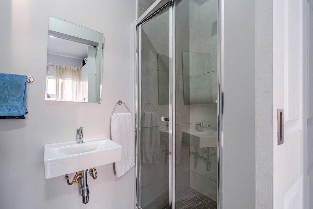 A compact, modern bathroom featuring a wall-mounted basin with chrome fixtures and a glass-enclosed shower with tiled flooring.