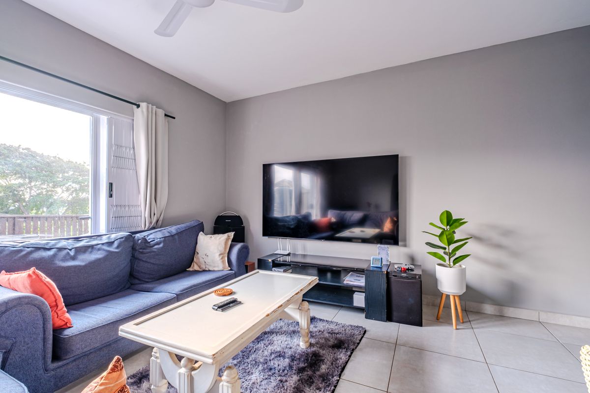 A bright living room featuring neutral grey walls, tiled flooring, a ceiling fan, and a sliding door providing access to the outdoor area.