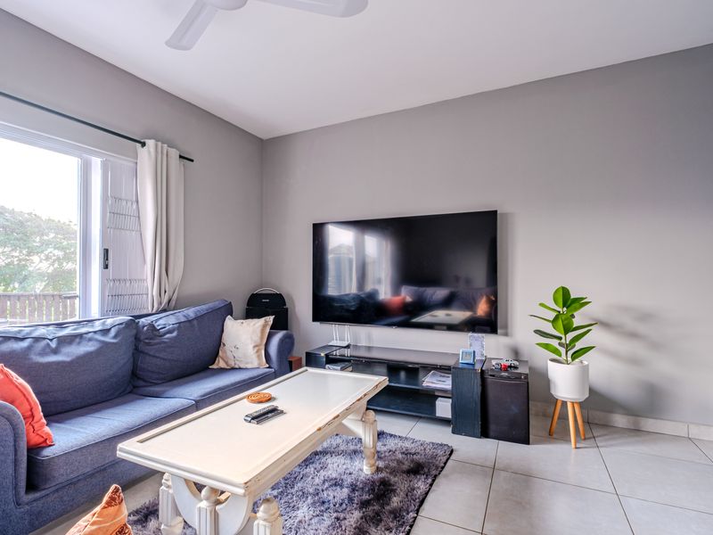 A bright living room featuring neutral grey walls, tiled flooring, a ceiling fan, and a sliding door providing access to the outdoor area.