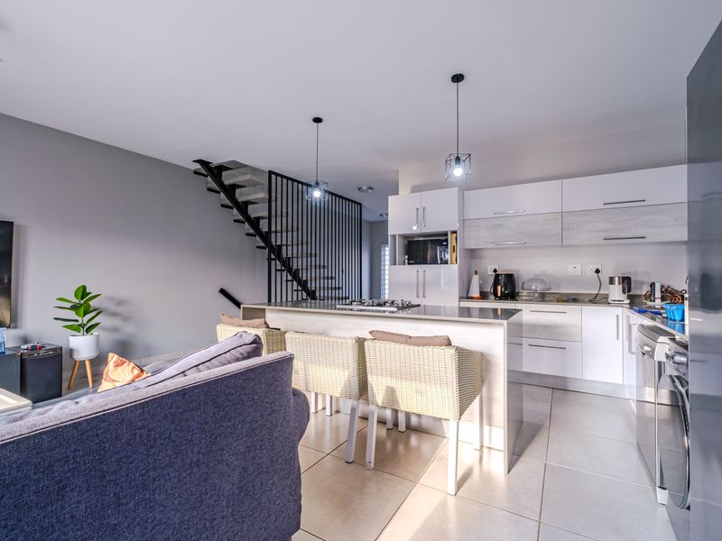 Modern open-plan living area featuring a sleek kitchen with built-in cabinetry, a central island, and a contemporary staircase with metal railings.